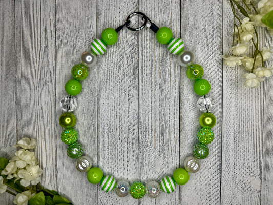 Beaded pet necklace with a lime and white pattern, including stripes. Displayed on a wooden surface with flowers for decoration. 