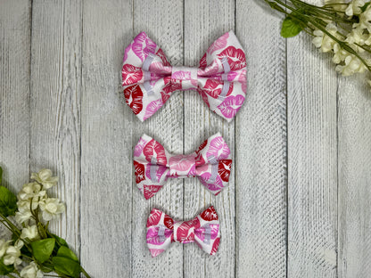 Picture of the backside of pet bow ties showing the elastic straps that fit around a collar. Displayed on a wooden surface with flowers for decoration. 