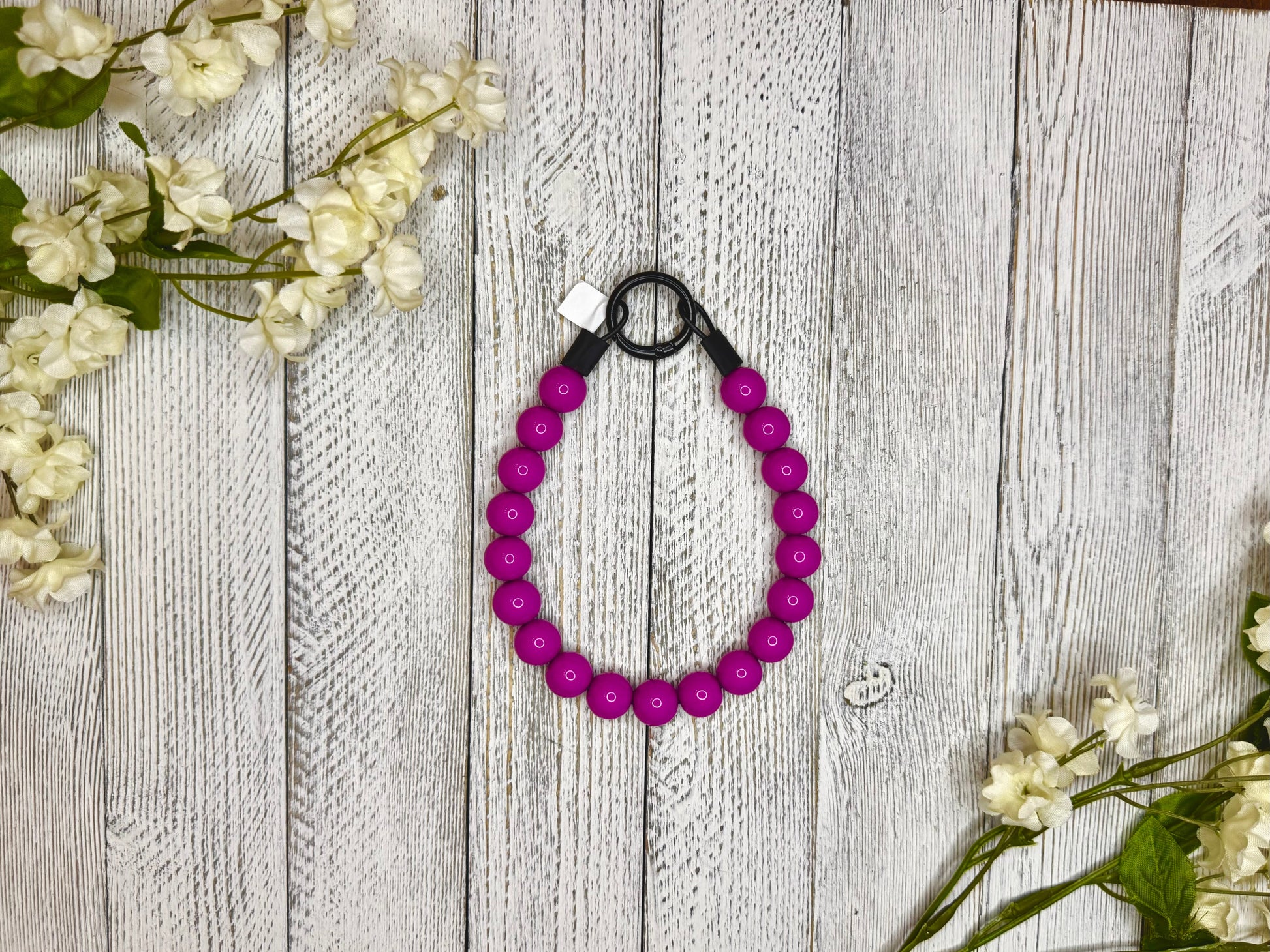 Beaded dog necklace with a magenta pattern. Displayed on a wooden surface with flowers for decoration.