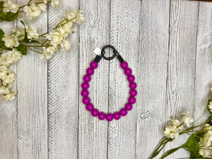 Beaded dog necklace with a magenta pattern. Displayed on a wooden surface with flowers for decoration.