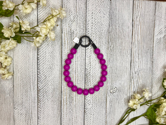 Beaded dog necklace with a magenta pattern. Displayed on a wooden surface with flowers for decoration.