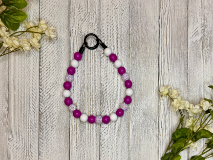 Beaded dog necklace with a magenta and white pattern. Displayed on a wooden surface with flowers for decoration.