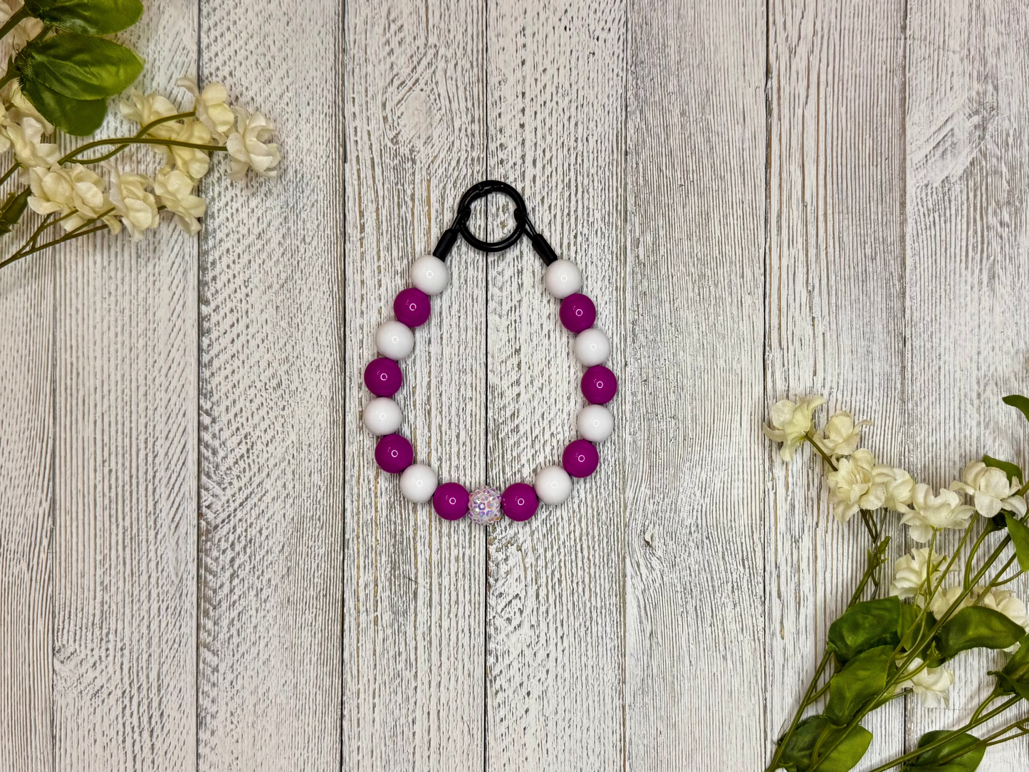 Beaded dog necklace with magenta and white pattern. Displayed on a wooden surface with flowers for decoration
