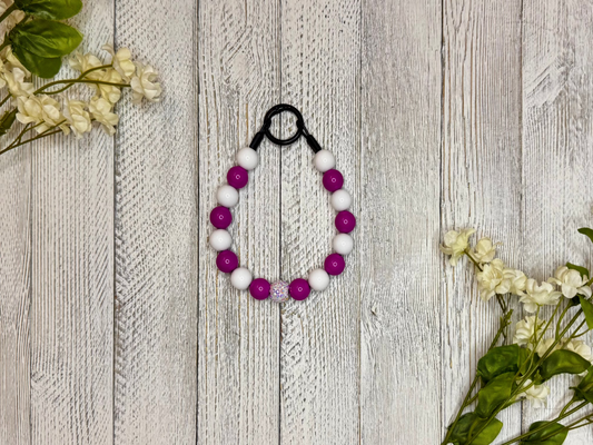 Beaded dog necklace with magenta and white pattern. Displayed on a wooden surface with flowers for decoration