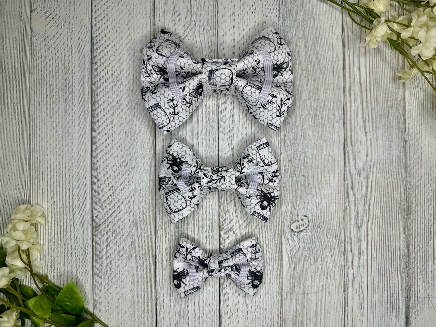 Picture of the backside of pet bow ties showing the elastic straps that fit around a collar. Displayed on a wooden surface with flowers for decoration. 