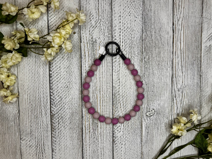 Beaded dog necklace with a light and dark mauve pattern. Displayed on a wooden surface with flowers for decoration.