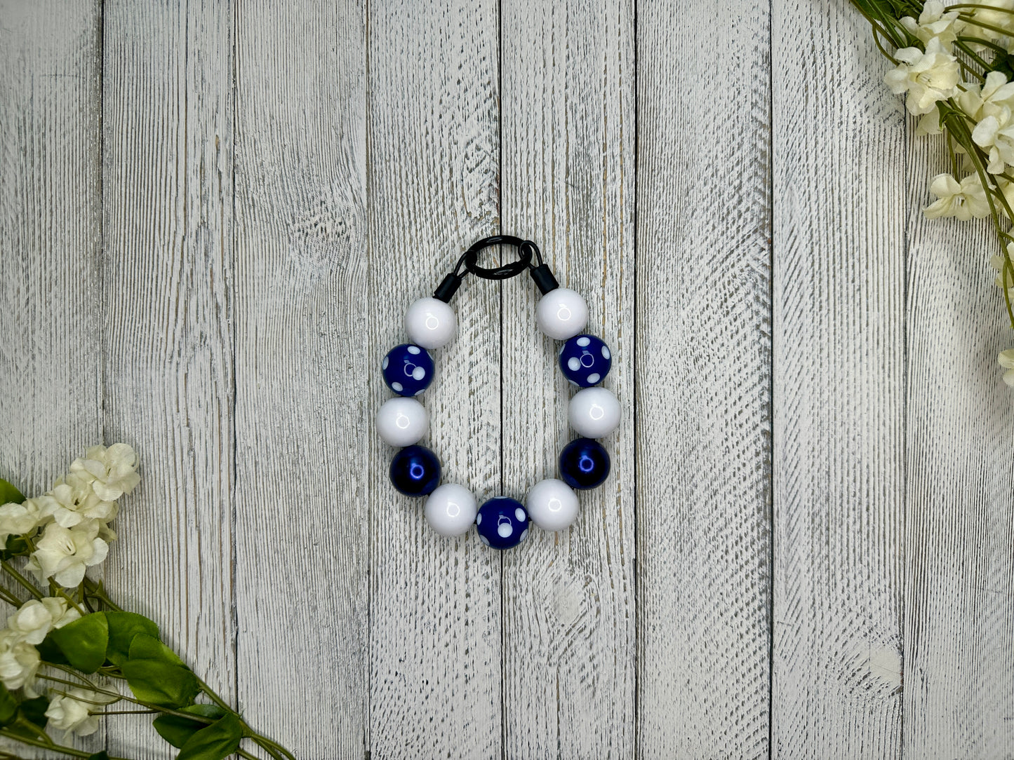 Beaded dog necklace with a navy and white pattern including polka dots. Displayed on a wooden surface with flowers for decoration. 