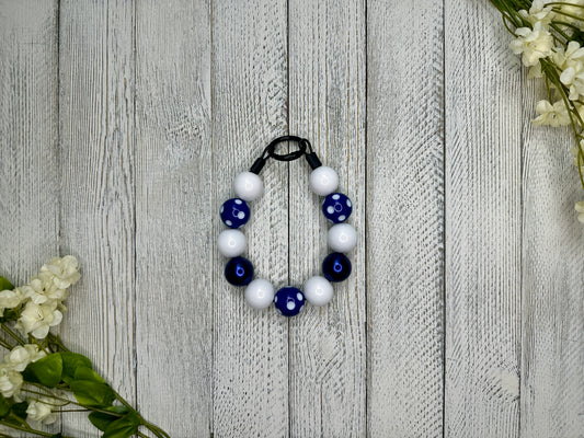 Beaded dog necklace with a navy and white pattern including polka dots. Displayed on a wooden surface with flowers for decoration. 