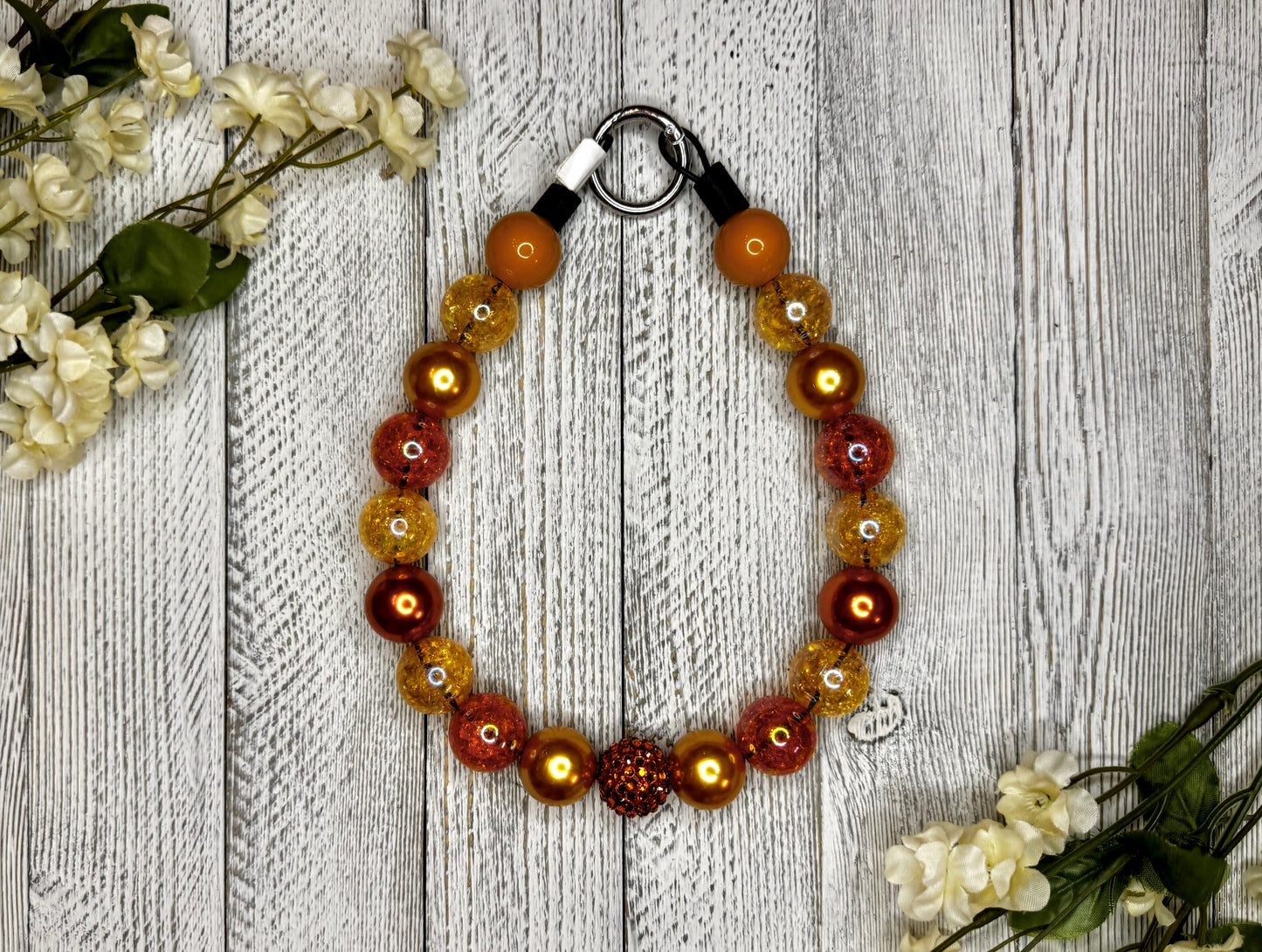 Beaded dog necklace with a shades of orange. Displayed on a wooden surface with flowers for decoration.