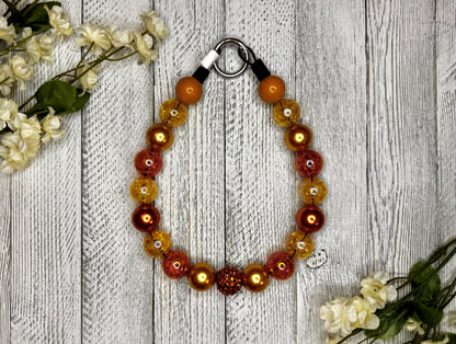 Beaded dog necklace with a shades of orange. Displayed on a wooden surface with flowers for decoration.