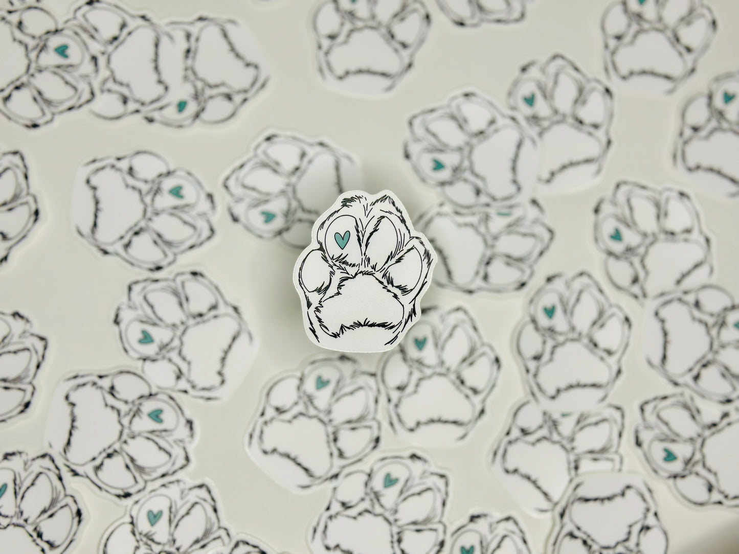 A sticker with a design of a paw print containing a blue heart in the center, placed on a background with the same paw print design.