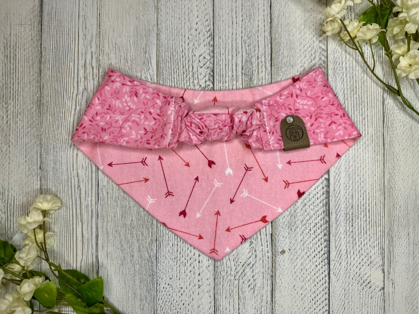Picture of the backside of a pet bandana showing the scrunchie neckline. Displayed on a wooden surface with flowers for decoration.