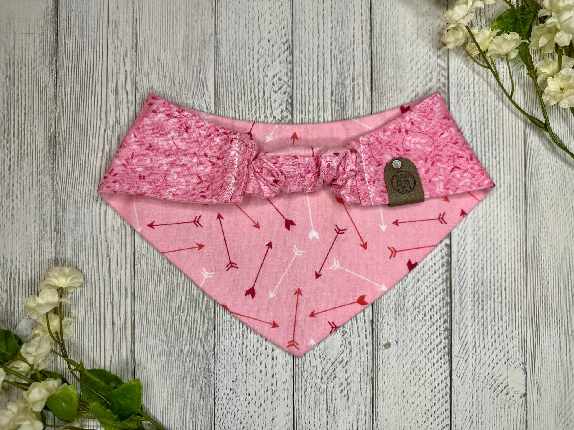 Picture of the backside of a pet bandana showing the scrunchie neckline. Displayed on a wooden surface with flowers for decoration.