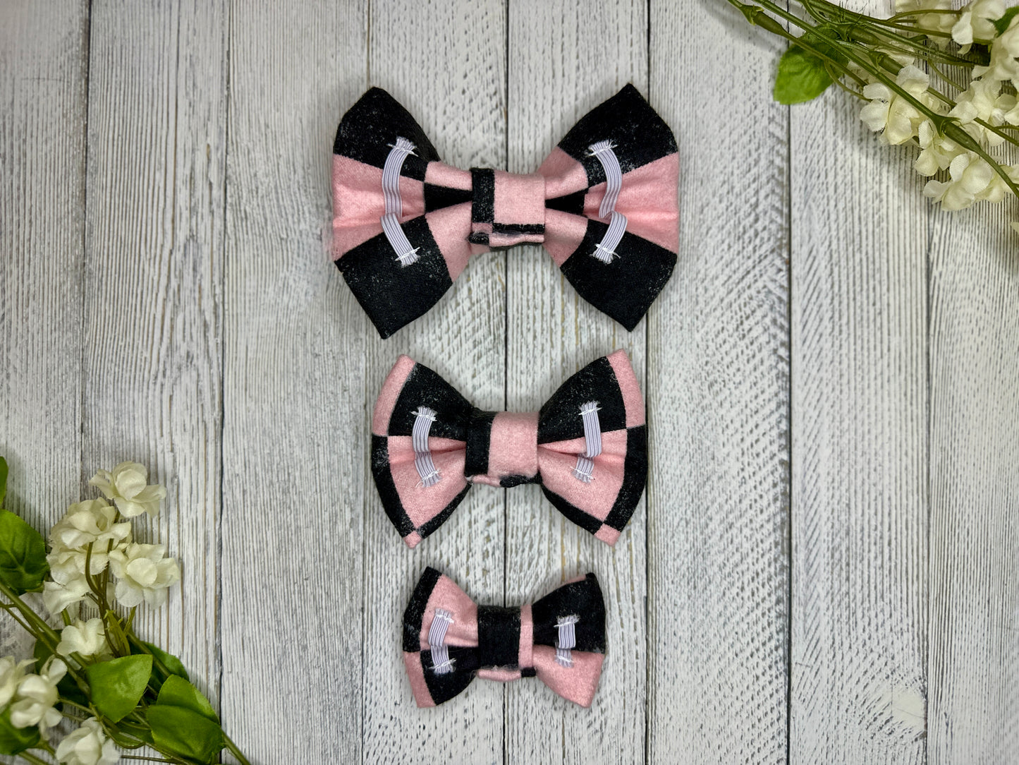 Picture of the backside of pet bow ties showing the elastic straps that fit around a collar. Displayed on a wooden surface with flowers for decoration. 