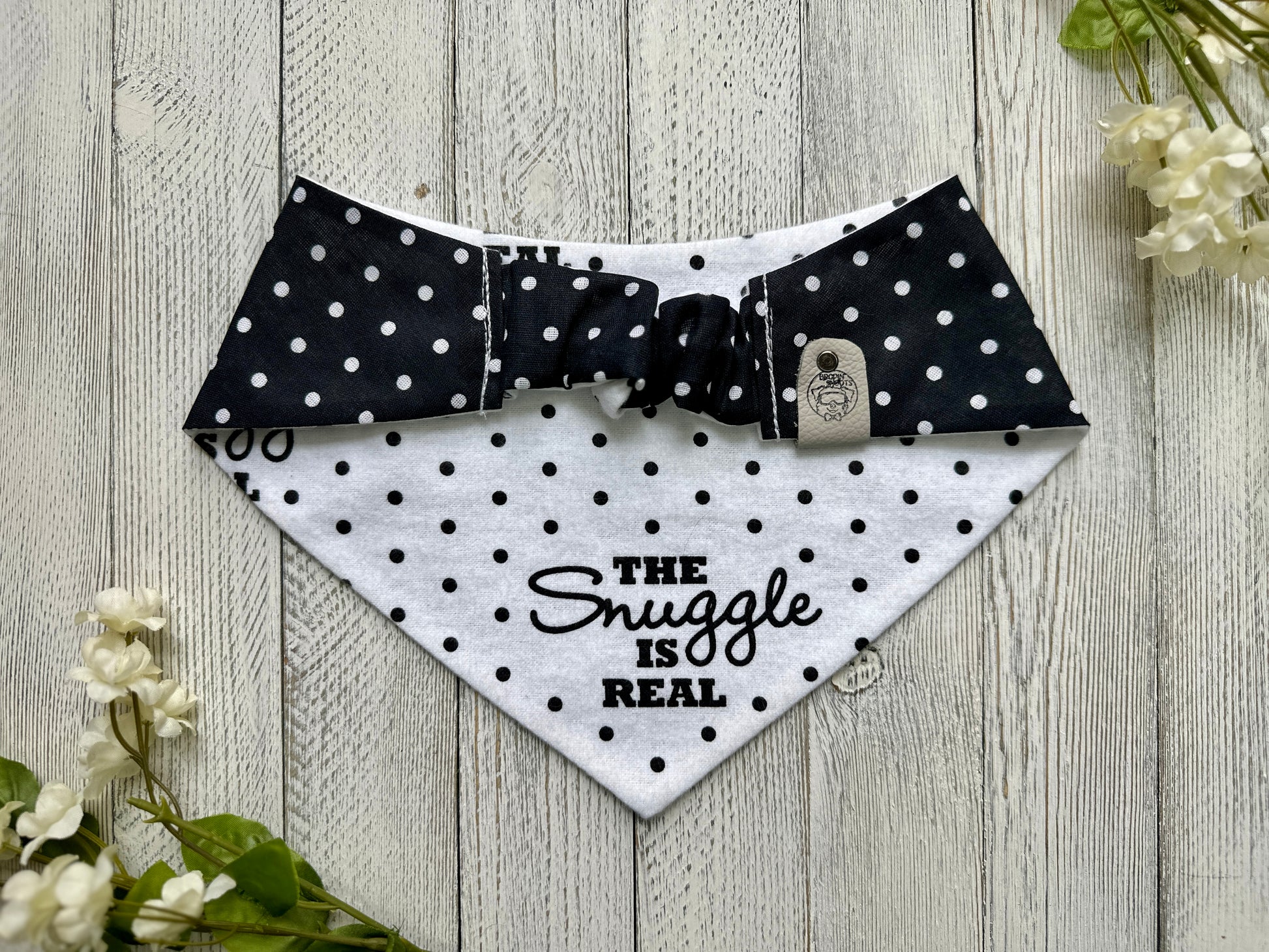 Picture of the backside of a pet bandana showing the scrunchie neckline. Displayed on a wooden surface with flowers for decoration. 