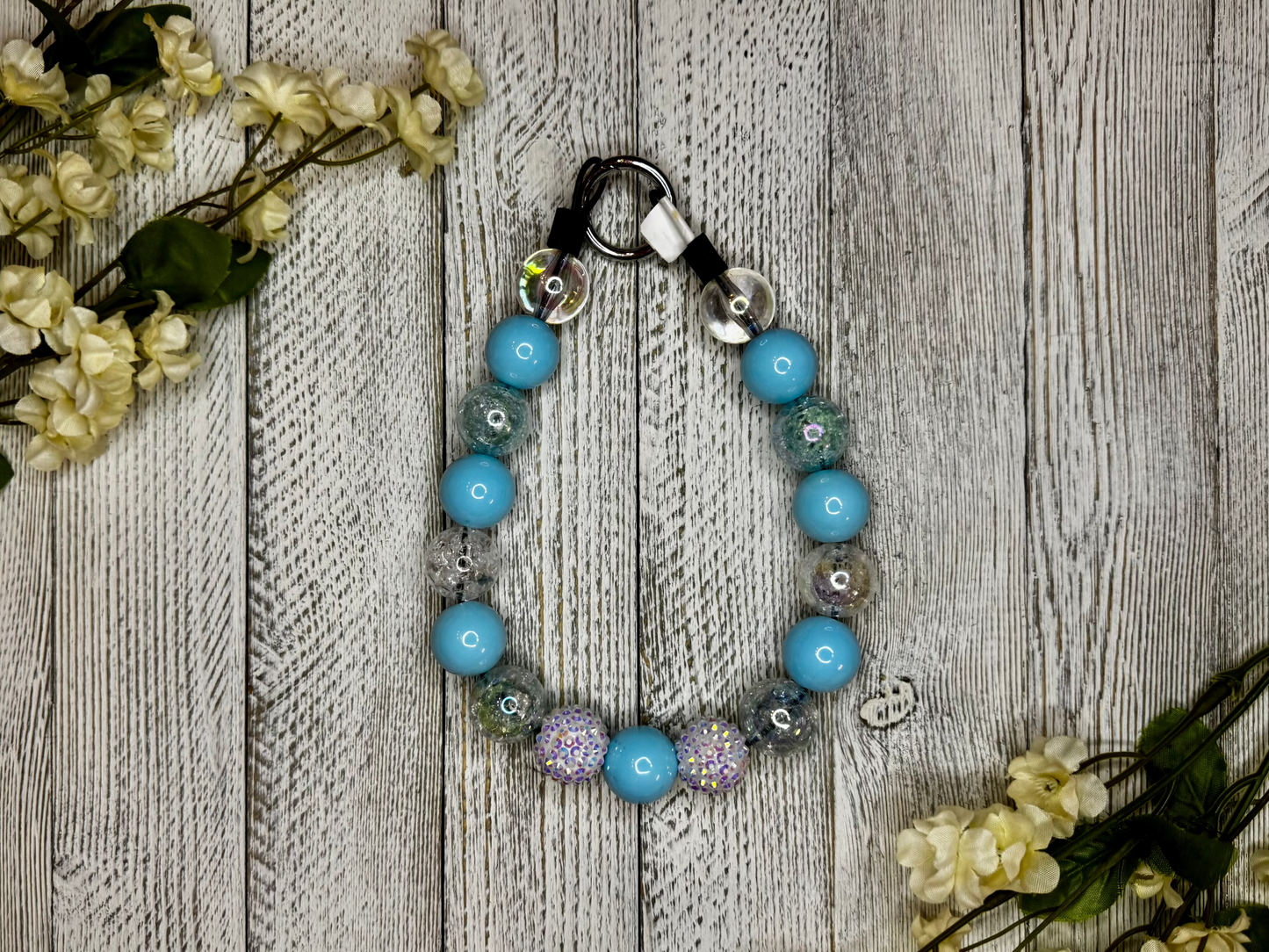 Beaded dog necklace with a blue and white pattern. Displayed on a wooden surface with flowers for decoration.
