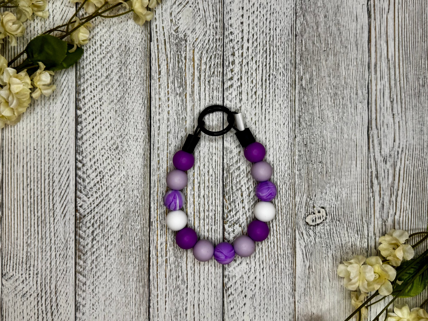 Beaded dog necklace with purple pattern including marble effect. Displayed on a wooden surface with flowers for decoration