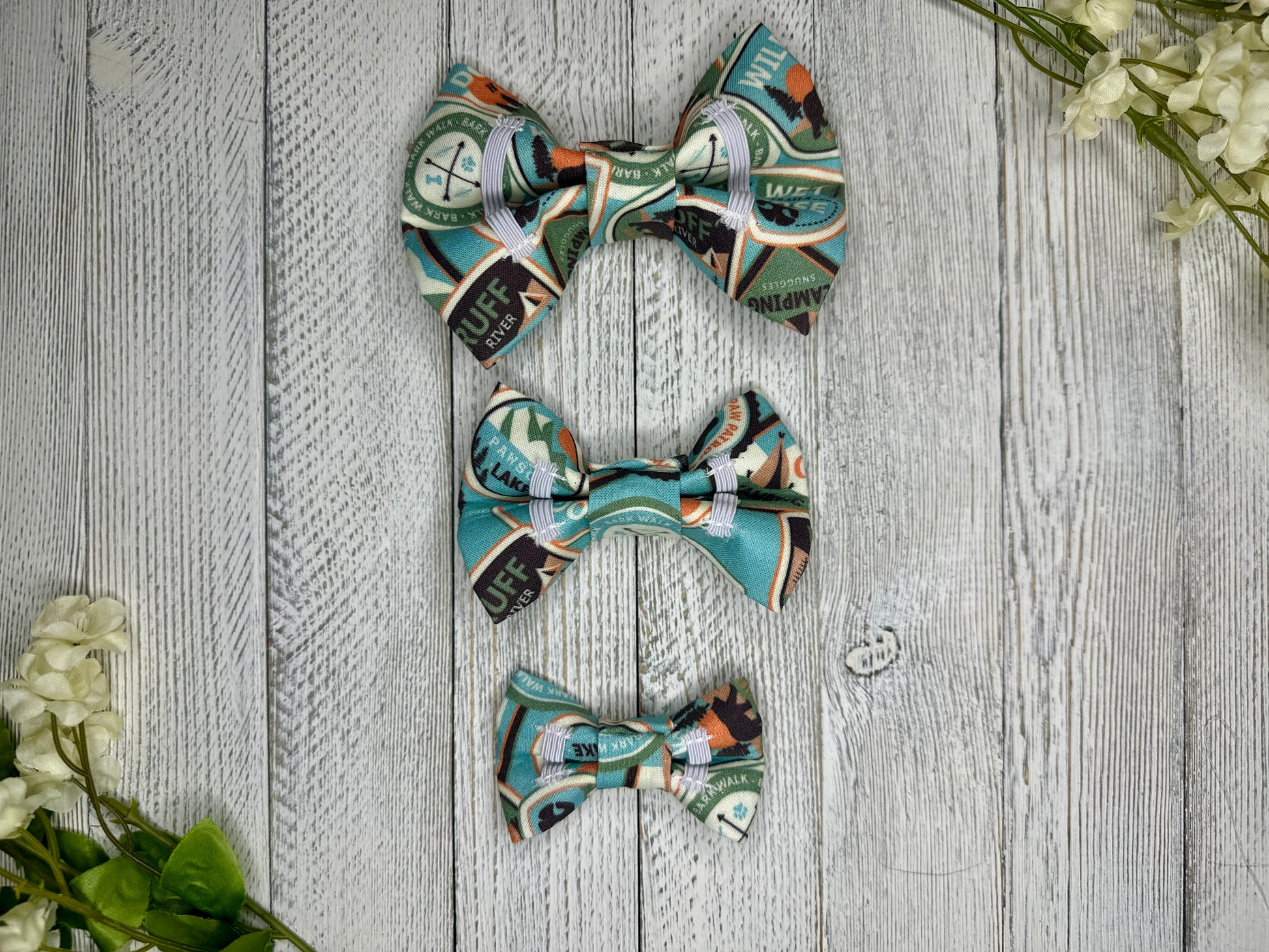 Picture of the backside of pet bow ties showing the elastic straps that fit around a collar. Displayed on a wooden surface with flowers for decoration.