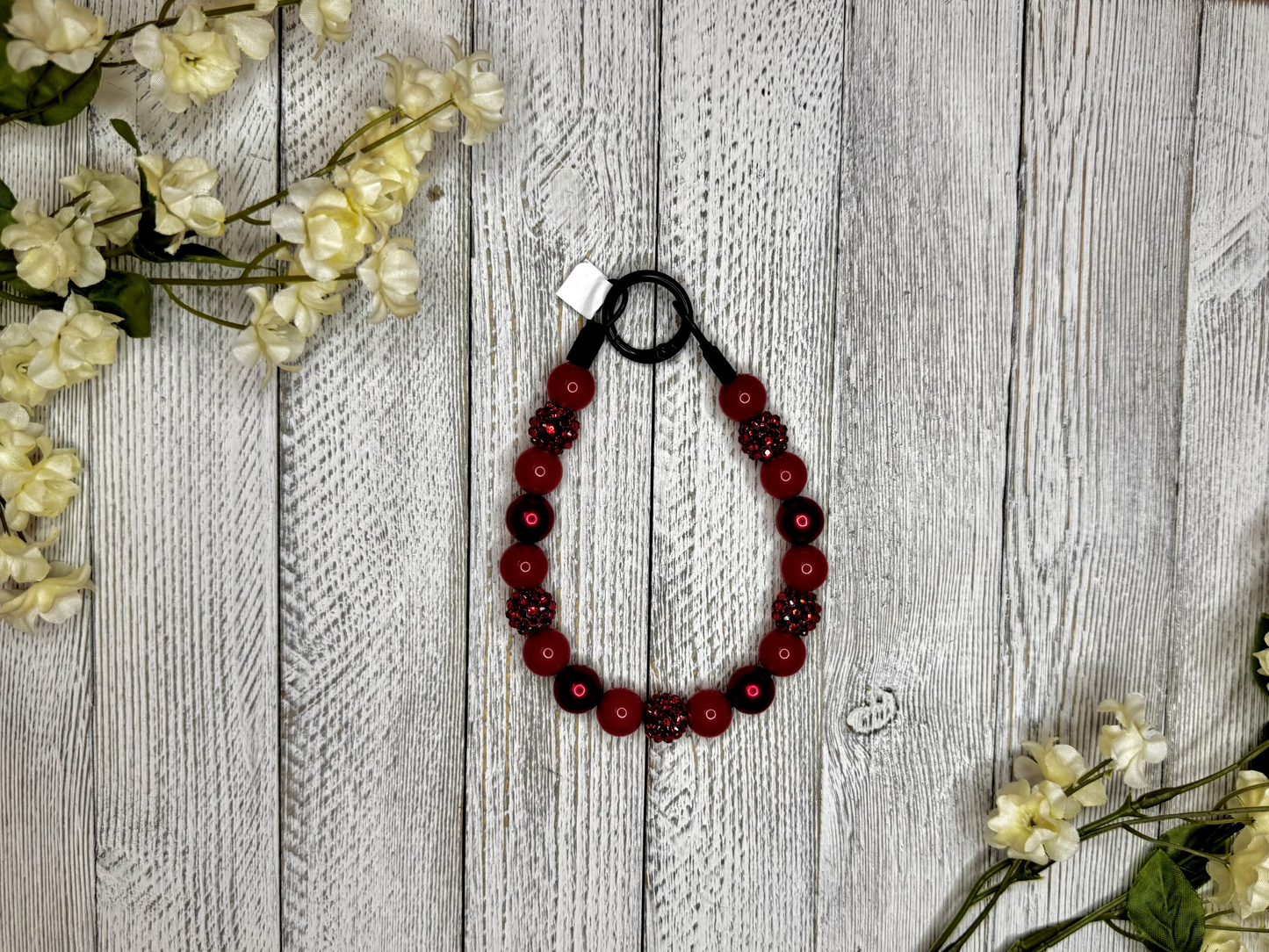 Beaded dog necklace with a red sparkle pattern. Displayed on a wooden surface with flowers for decoration.