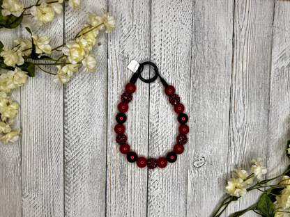 Beaded dog necklace with a red sparkle pattern. Displayed on a wooden surface with flowers for decoration.