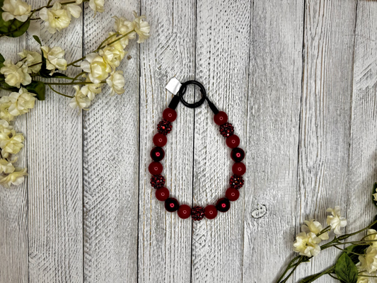 Beaded dog necklace with a red sparkle pattern. Displayed on a wooden surface with flowers for decoration.