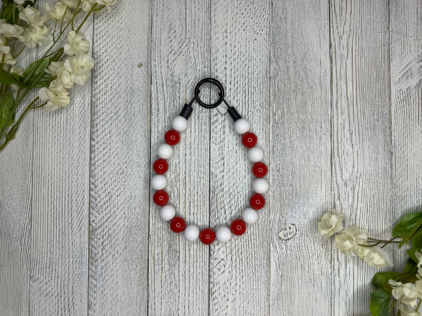 Beaded dog necklace with a red and white pattern. Displayed on a wooden surface with flowers for decoration.