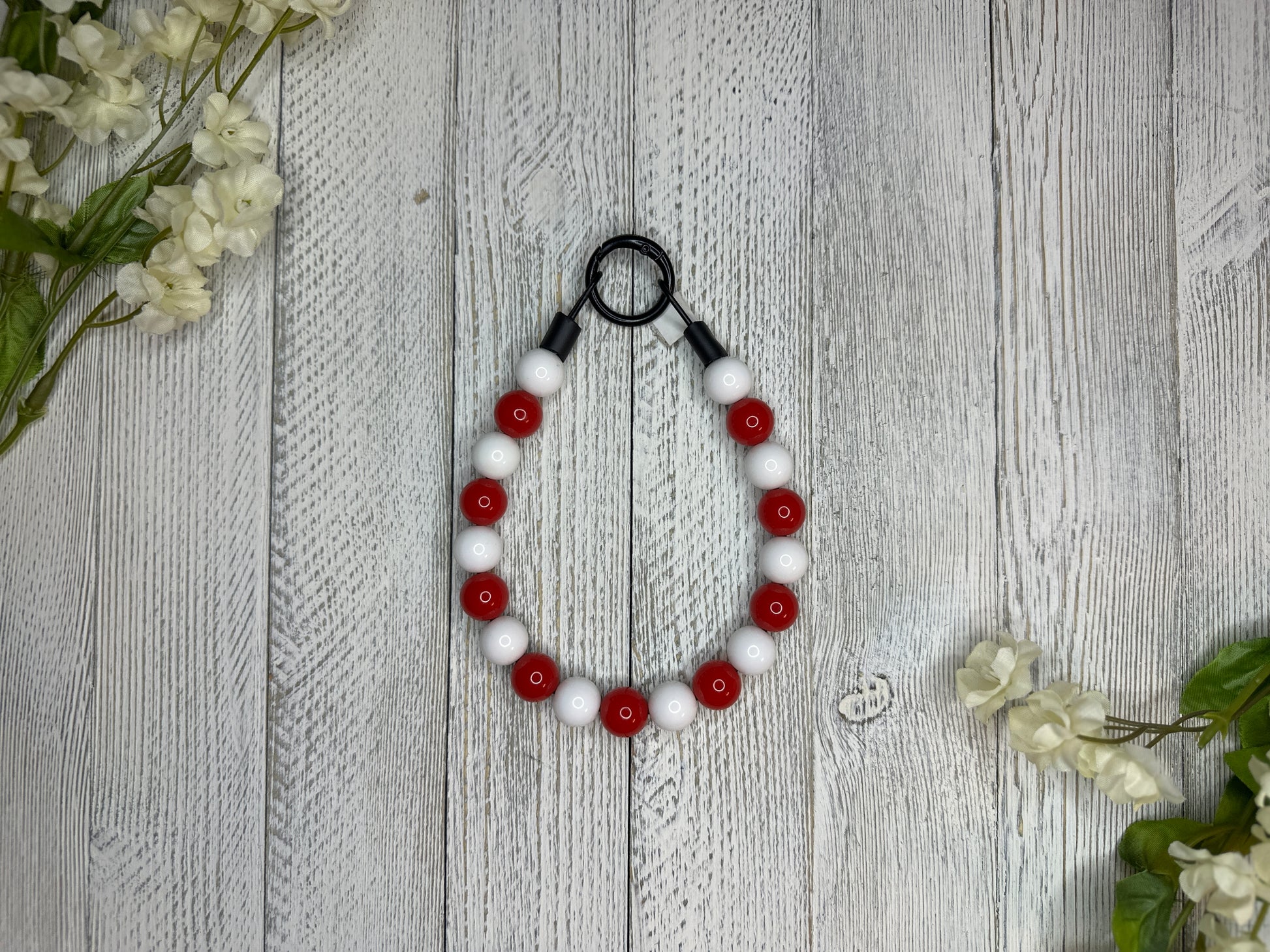 Beaded dog necklace with a red and white pattern. Displayed on a wooden surface with flowers for decoration.