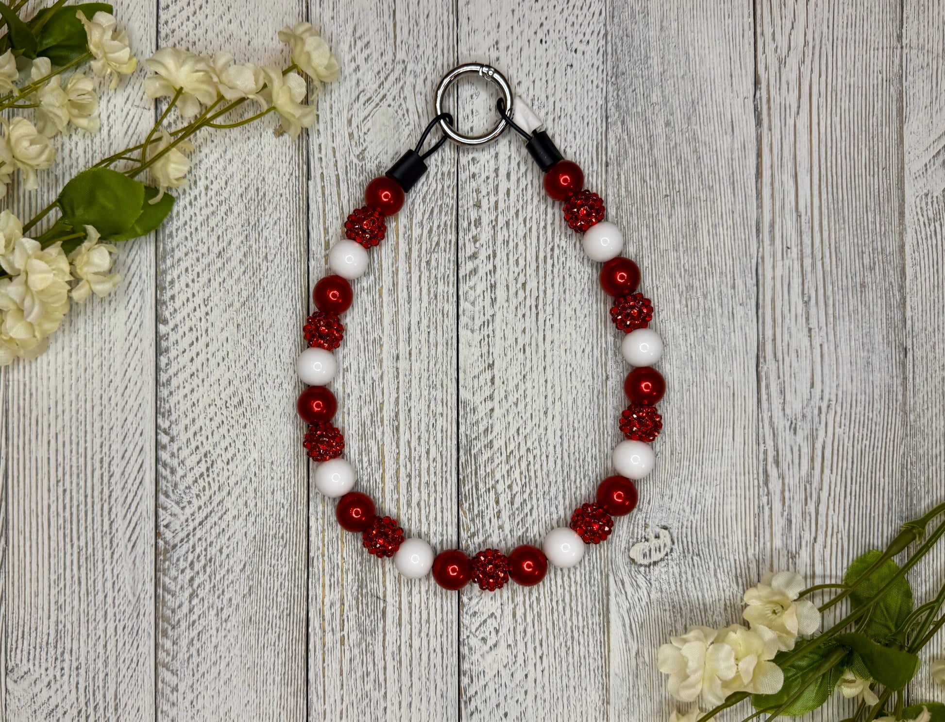 Beaded dog necklace with a red and white pattern. Displayed on a wooden surface with flowers for decoration.