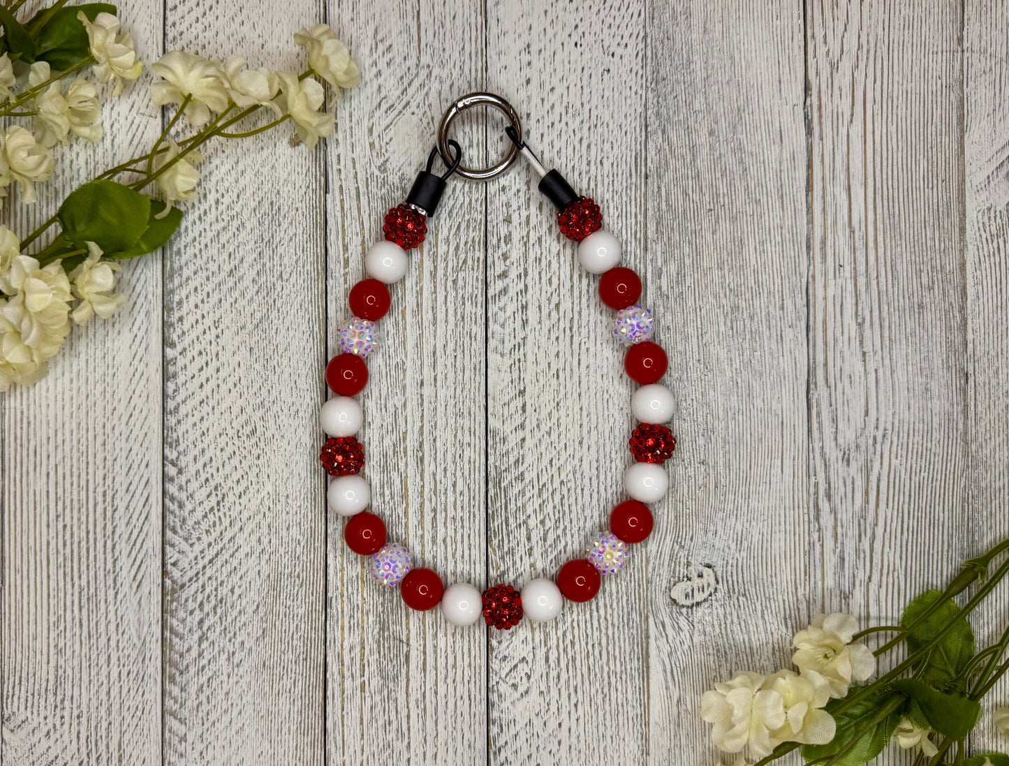 Beaded pet necklace with a red and white pattern. Displayed on a wooden surface with flowers for decoration. 