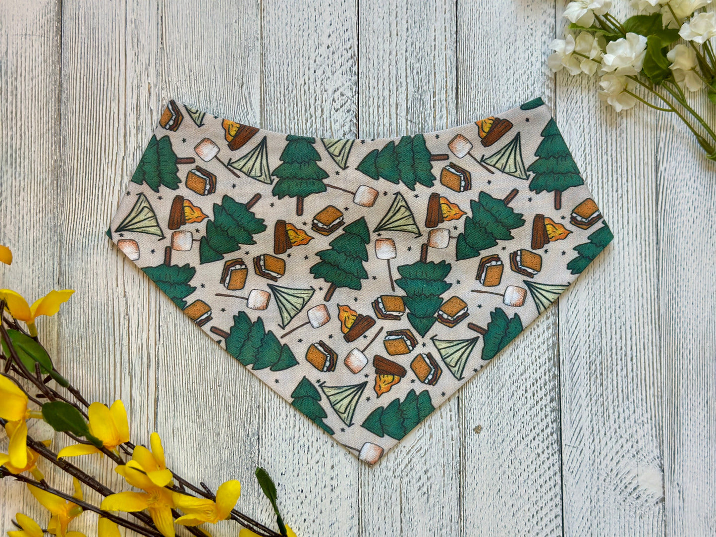 Pet bandana with camping-themed pattern on a wooden surface with flowers.