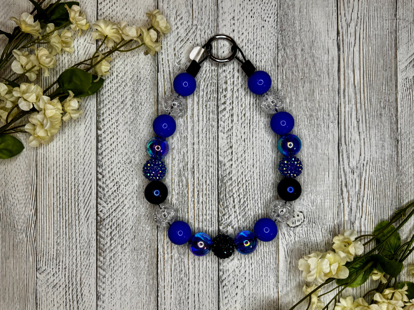 Beaded dog necklace with a sparkly blue pattern. Displayed on a wooden surface with flowers for decoration.
