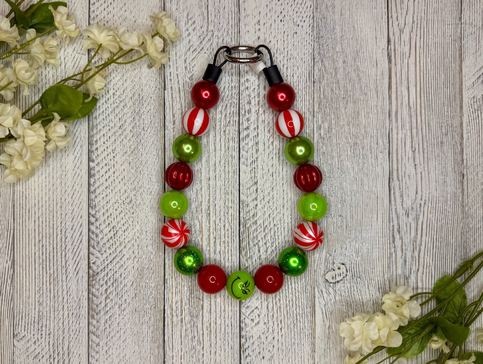 Beaded dog necklace with a red and green pattern including candy cane swirls. Displayed on a wooden surface with flowers for decoration.