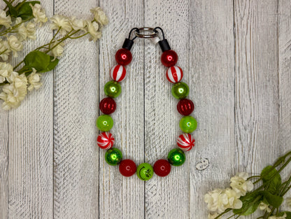 Beaded dog necklace with a red and green pattern including candy cane swirls. Displayed on a wooden surface with flowers for decoration.
