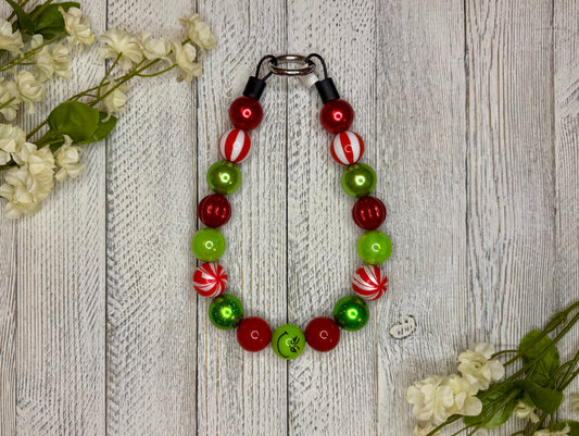Beaded dog necklace with a red and green pattern including candy cane swirls. Displayed on a wooden surface with flowers for decoration.
