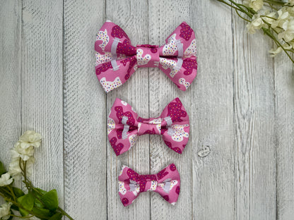 Picture of the backside of pet bow ties showing the elastic straps that fit around a collar. Displayed on a wooden surface with flowers for decoration. 