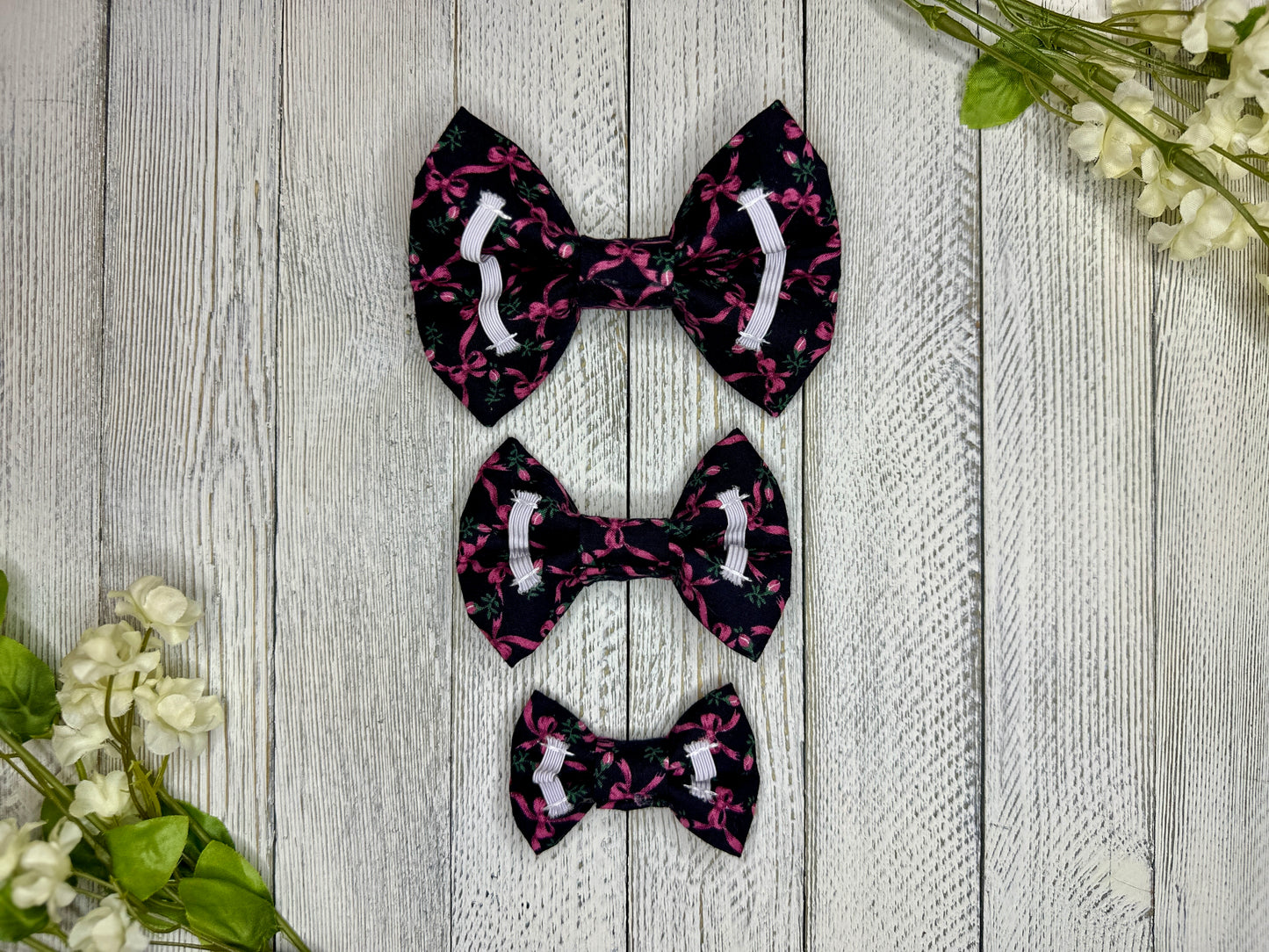 Picture of the backside of pet bow ties showing the elastic straps that fit around a collar. Displayed on a wooden surface with flowers for decoration. 