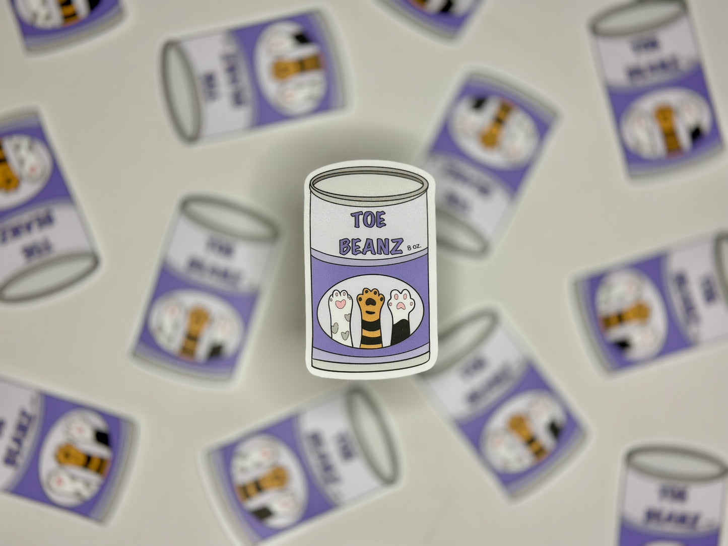 Sticker showing a can with a label with cap paws and a label that says toe beanz