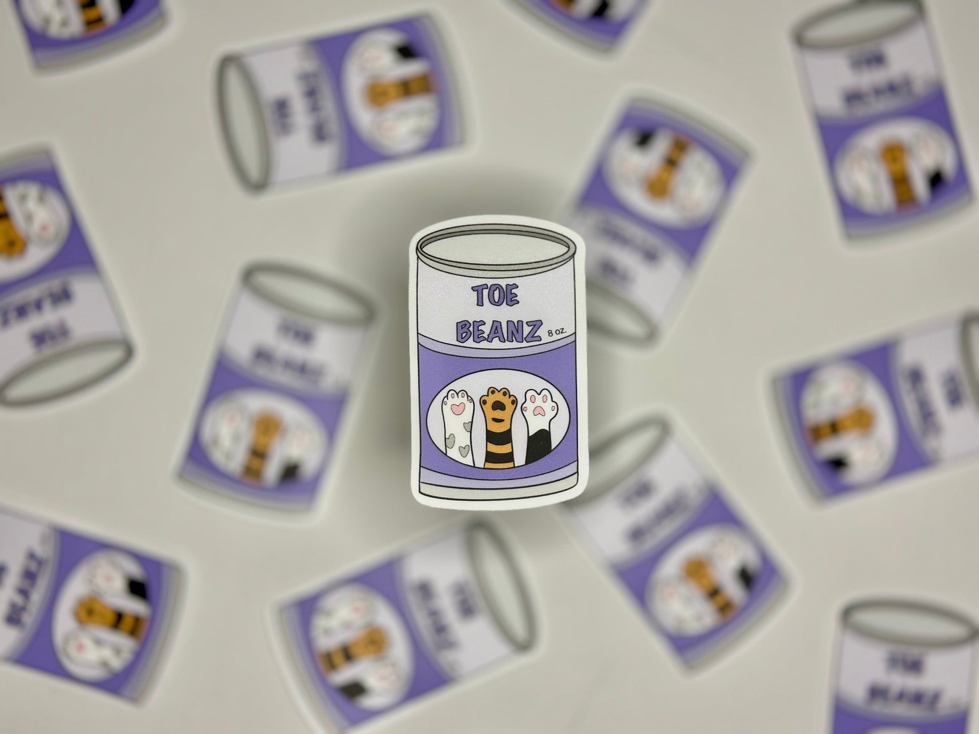 Sticker showing a can with a label with cap paws and a label that says toe beanz