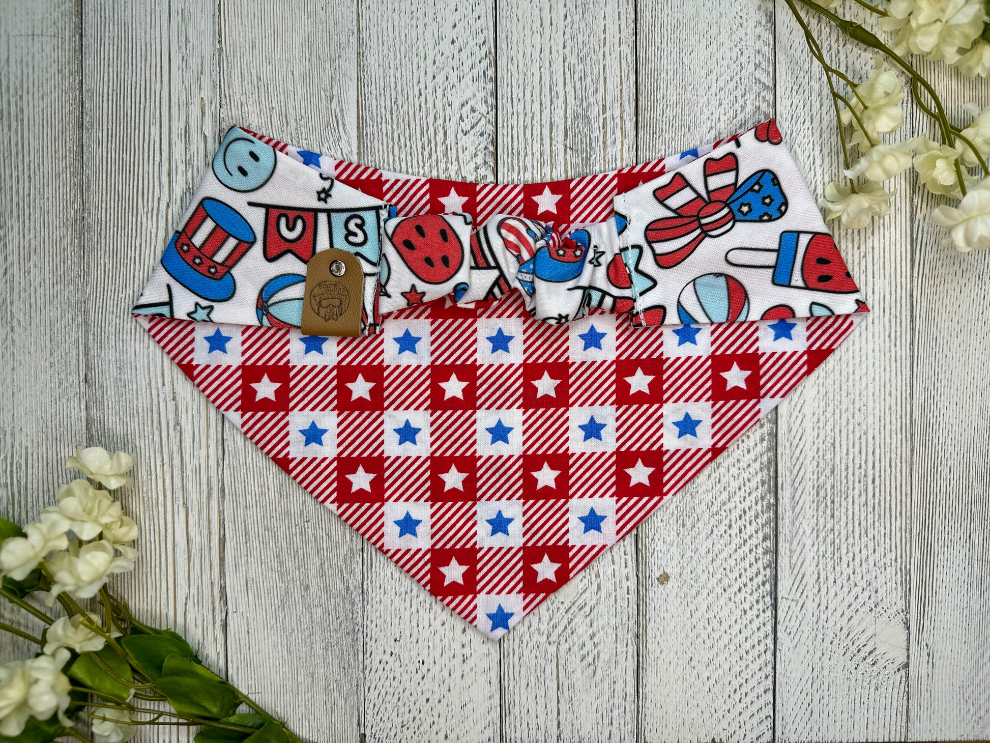 Picture of the backside of a pet bandana showing the scrunchie neckline. Displayed on a wooden surface with flowers for decoration. 
