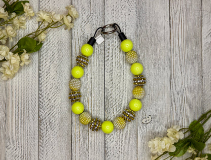 Beaded dog necklace with a yellow pattern including sparkles. Displayed on a wooden surface with flowers for decoration.