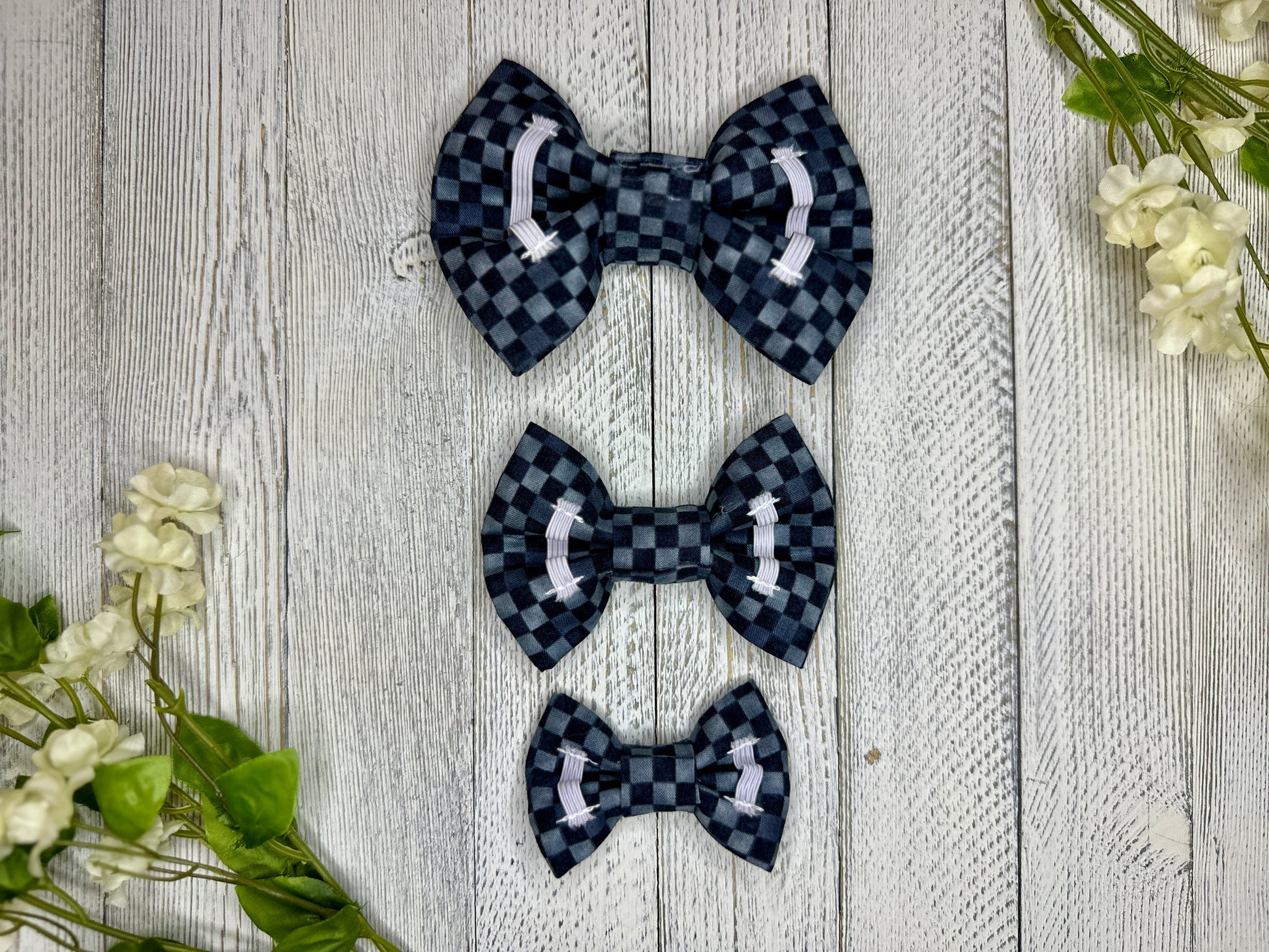 Picture of the backside of pet bow ties showing the elastic straps that fit around a collar. Displayed on a wooden surface with flowers for decoration. 