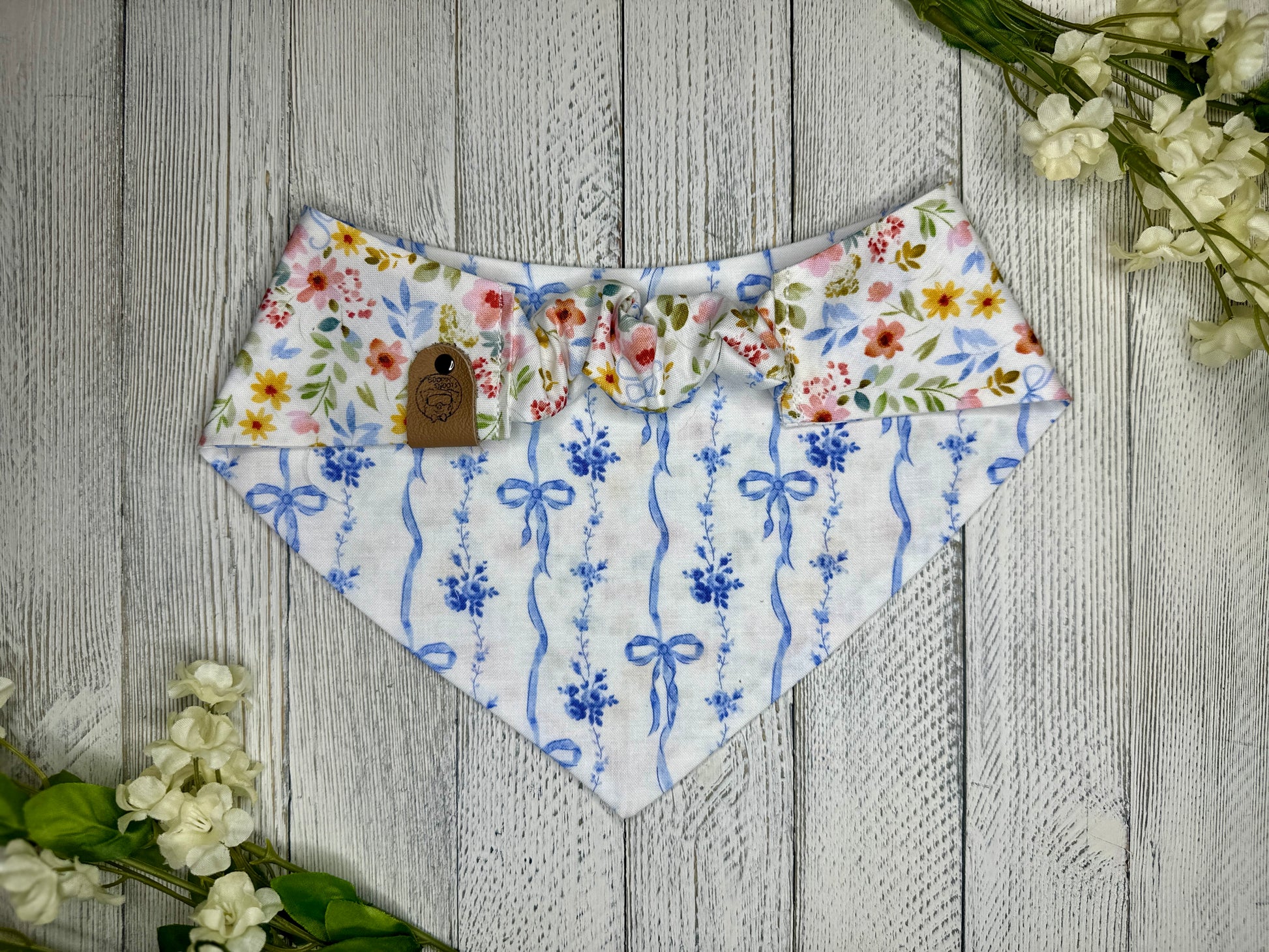 Picture of the backside of a pet bandana showing the scrunchie neckline. Displayed on a wooden surface with flowers for decoration. 