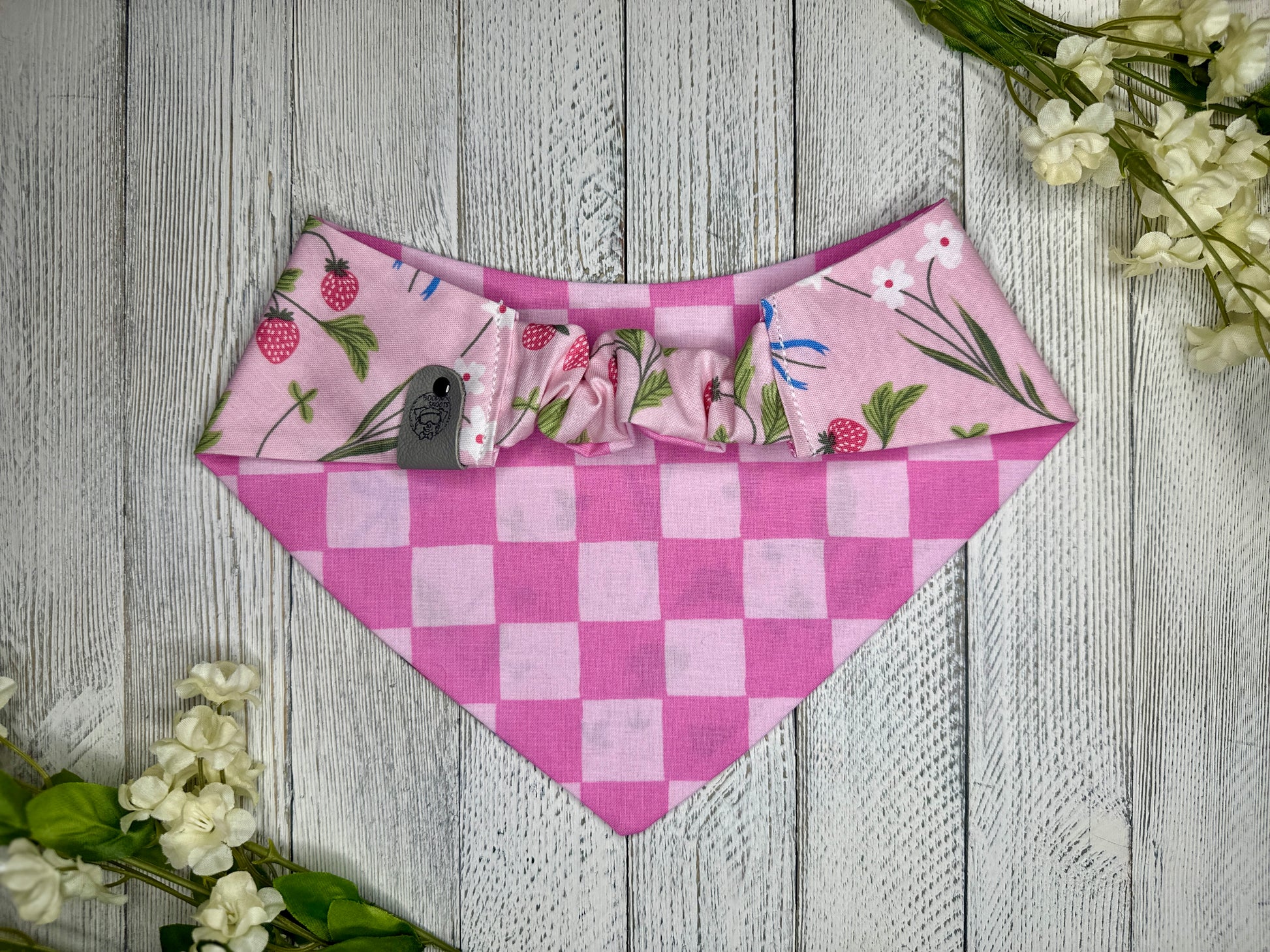 Picture of the backside of a pet bandana showing the scrunchie neckline. Displayed on a wooden surface with flowers for decoration. 