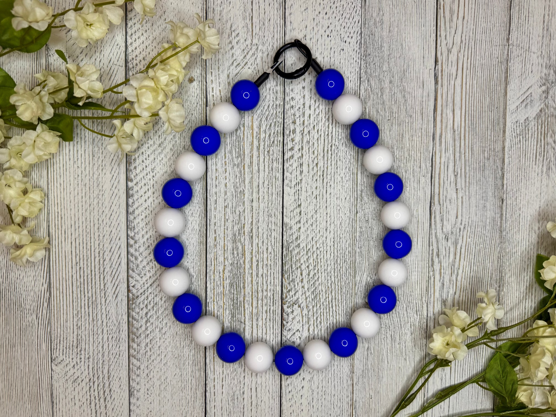 Beaded pet necklace with a blue and white pattern. Displayed on a wooden surface with flowers for decoration. 