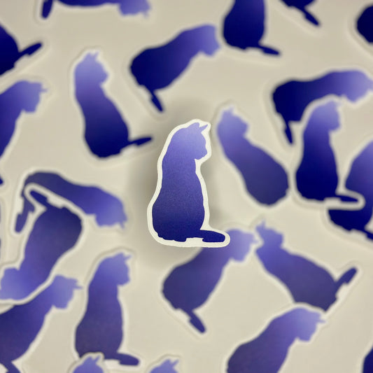 A blue vinyl sticker in the shape of a cat's silhouette, surrounded by other similar stickers in the background.