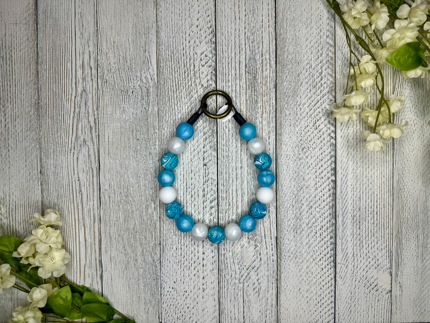 Beaded pet necklace with a blue and white pattern. Displayed on a wooden surface with flowers for decoration. 