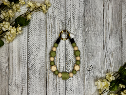 Beaded pet necklace with a olive green and tan pattern, including a rainbow. Displayed on a wooden surface with flowers for decoration. 