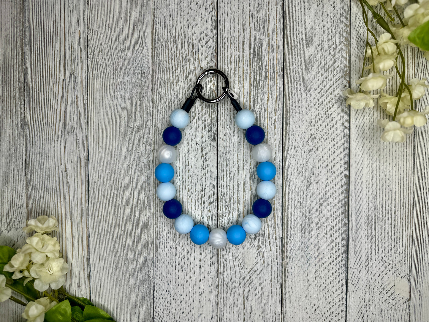 Beaded pet necklace with a blue and white pattern. Displayed on a wooden surface with flowers for decoration. 