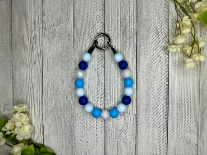 Beaded pet necklace with a blue and white pattern. Displayed on a wooden surface with flowers for decoration. 