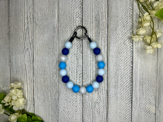 Beaded pet necklace with a blue and white pattern. Displayed on a wooden surface with flowers for decoration. 